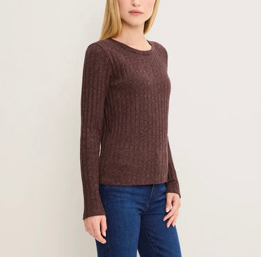 A woman wearing a ribbed long-sleeve crewneck sweater in a dark brownish-purple color, paired with blue jeans, against a plain light background.
