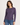 A woman modeling a heathered purple long-sleeve top with a gathered side detail, paired with blue jeans, against a plain light background.