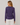 A woman shown from the back wearing a heathered purple long-sleeve top with a ruched side detail and white pants, set against a plain light gray studio background.