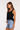 Woman wearing a black sleeveless top and blue denim shorts on a white background