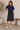 A woman wearing a black shirred waistband a-line midi skirt and a navy top on a neutral background