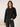 A woman modeling a black cropped crewneck sweatshirt with white stripes down the sleeves, paired with dark gray jeans, against a neutral cream background.