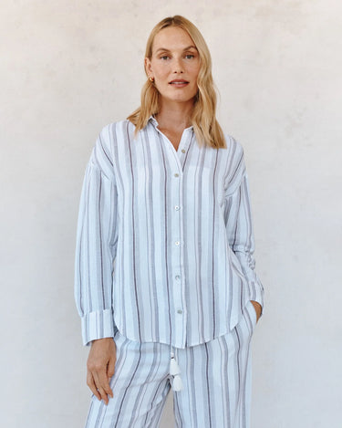 Woman wearing a light blue and white striped pajama set against a plain background