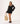 A model wearing a black dress under a black lace long-sleeve tunic cover-up with scalloped pattern, lace-up V-neck and tassel ties.