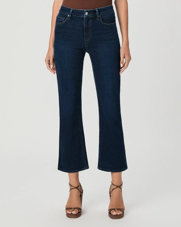 A model wearing dark blue cropped flare jeans with a brown top and brown strappy high-heeled sandals, shown from the waist down on a light gray studio background.