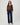 A woman modeling a brown long-sleeve button-front blouse with gathered cuffs and dark blue wide-leg jeans, standing against a light gray studio background.
