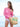 Woman in pink sweater and white shorts holding a straw bag with floral designs on a beach.