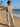 Woman in striped outfit standing on a beach with ocean and palm trees in the background