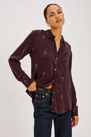 a woman wearing a burgundy blouse with Martin glasses printed on and dark blue denim on a white background.