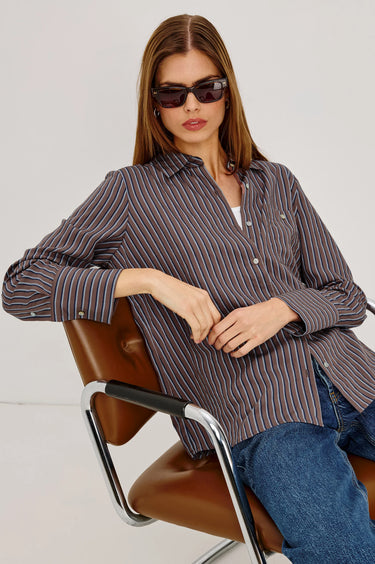 Woman wearing a striped shirt and sunglasses sitting on a chair with a white background