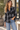 a woman wearing a black and ivory plaid collared shirt and blue jeans on a outside background