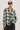 A woman modeling a long-sleeve plaid button-up shirt in white, green, and gray, paired with dark jeans and sunglasses, against a plain light background.