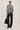 Person wearing a green and black plaid shirt with black jeans, holding a black bag on a white background