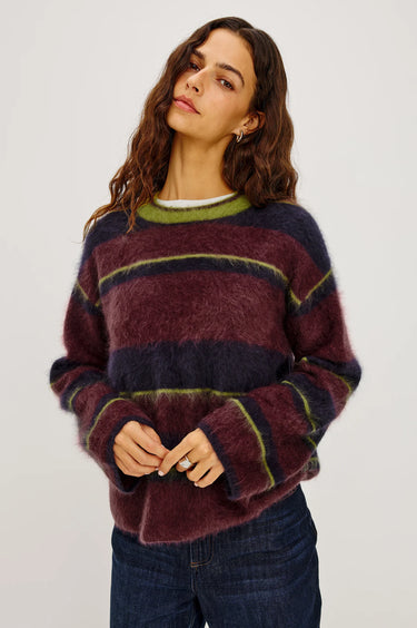 A woman wearing a burgundy, navy and green stripe brushed wool crew neck sweater and dark blue denim jeans on a white background