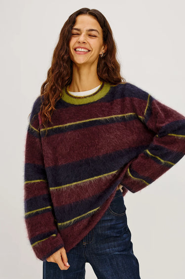 A woman wearing a burgundy, navy and green stripe brushed wool crew neck sweater and dark blue denim jeans on a white background