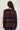A woman wearing a burgundy, navy and green stripe brushed wool crew neck sweater and dark blue denim jeans on a white background