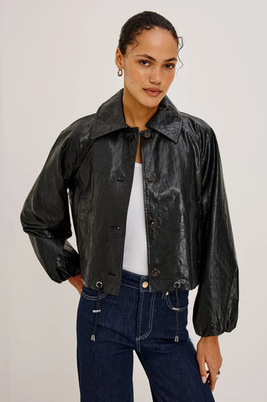 A woman wearing a black faux leather jacket, a white tee, and dark blue denim on a white background.