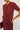 A close-up of a model wearing a short-sleeve fuzzy knit cardigan and matching satin skirt in a deep burgundy red, holding a matching clutch.