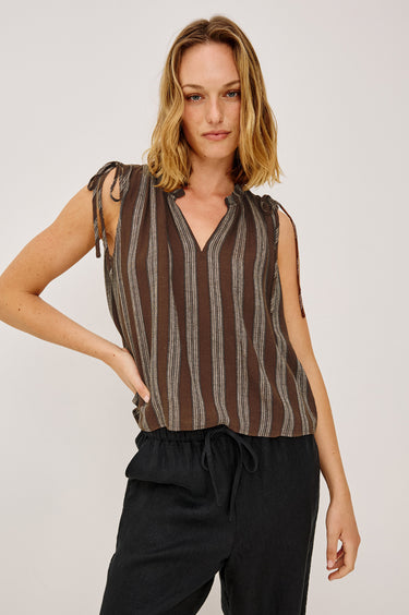Woman wearing a brown striped sleeveless top and black pants on a white background