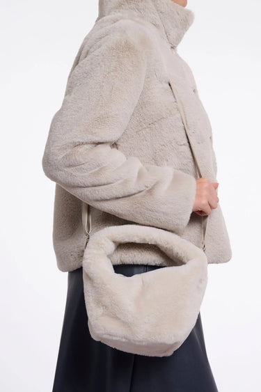 A person wearing a light beige fuzzy shearling-style jacket and a matching fuzzy crescent shoulder bag, shown in side profile against a plain white background.