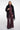 A woman modeling a black fringed faux-fur cape over a matching dark plum satin top and wide-leg trousers, photographed against a light gray studio background.