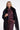 A blonde model wearing a black fringed faux-fur cape over a matching dark plum satin blouse and trousers, photographed against a plain light gray studio background.
