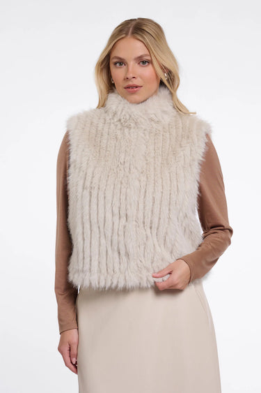 Woman wearing a beige fur vest over a brown long-sleeve top on a white background