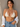 Woman wearing a beige bikini top and blue jeans against a neutral wall