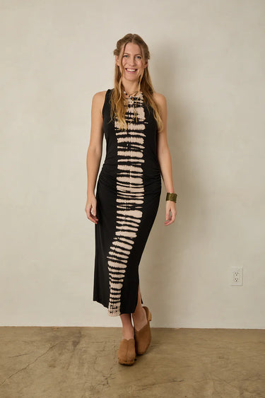 Woman wearing a sleeveless dress with tie-dye pattern against a plain wall.