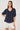 Woman wearing a navy striped blouse with white buttons and white shorts on a light background