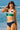 Woman wearing a green and navy bikini standing on a beach with ocean waves in the background