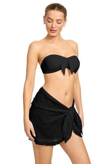 Woman wearing a black strapless top and black sarong on a white background