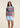 A woman wearing a zig zag stripe polo in multi color with blue shorts on a neutral background