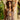 Woman in a patterned dress leaning against a stone column with greenery in the background