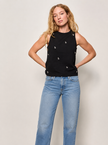 Woman wearing a black sleeveless top with embellished front and blue jeans against a plain background