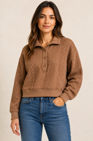 A woman wearing a brown cable-knit polo sweater with a button placket and blue jeans, standing against a plain beige studio background.