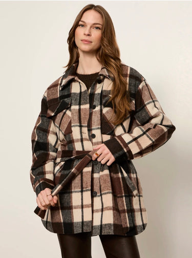 A woman modeling a long-sleeve belted plaid coat in brown, beige, and black tones, paired with dark brown leggings, against a plain light gray studio background.