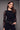 A woman wearing a black long sleeve floral mesh top and black pants on a grey studio background