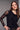 A woman wearing a black long sleeve floral mesh top and black pants on a grey studio background