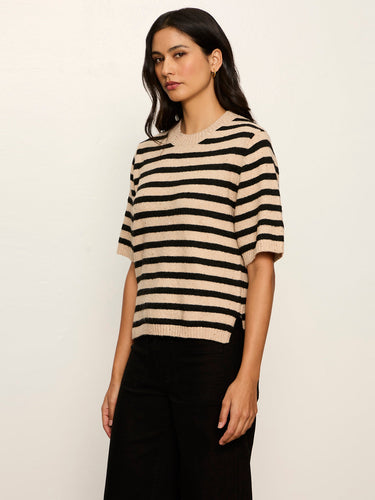 A woman modeling a short-sleeve knit sweater with horizontal beige and black stripes, paired with black pants, against a plain off-white background.