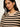 A close-up of a woman wearing a beige knit sweater with horizontal black stripes and small scattered sequins, paired with a gold hoop earring, against a plain light background.