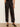 Black wide-leg trousers with a satin-like sheen, shown on a model wearing black slingback heels against a neutral studio background.