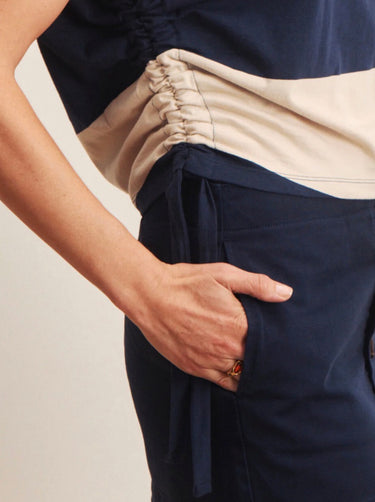 A woman wearing a rugby-reminicient striped shirt in navy and opal with ruched side details and a navy blue skirt