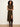 A woman modeling a sleeveless high-neck midi dress with a black and tan plaid pattern and a thigh-high slit, paired with dark brown knee-high boots against a plain off-white studio background.