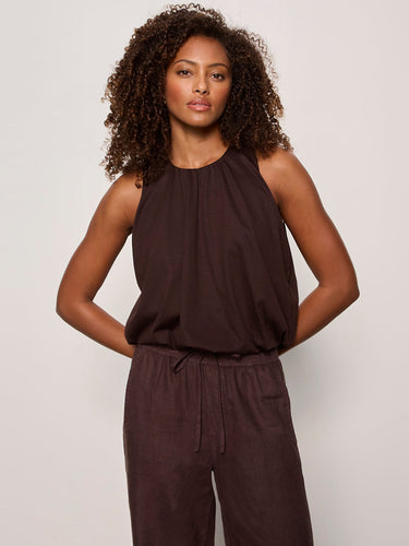 Woman wearing a brown sleeveless top and pants against a plain background
