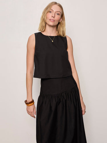 Woman wearing a black sleeveless top and black skirt against a plain background