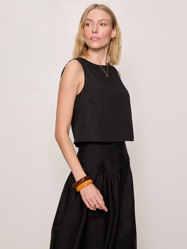Woman wearing a black sleeveless top and black pants against a plain background