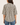 A woman viewed from the back wearing a short-sleeve button-up blouse with a black and cream ikat-style vertical pattern, paired with blue jeans, against a solid light beige background.