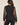 A woman shown from the back wearing a black leopard-print long-sleeve blouse with sheer mesh sleeves and black jeans, against a plain light beige studio background.