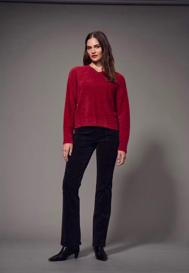 a woman wearing a brushed v-neck red sweater and black jeans on a grey studio background.